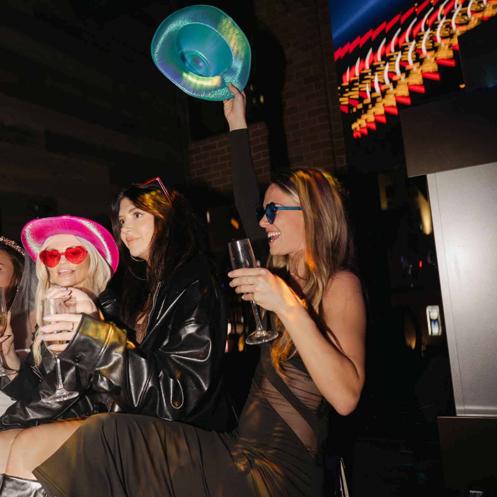 Group of women having fun, raising hats and glasses while enjoying a lively night out