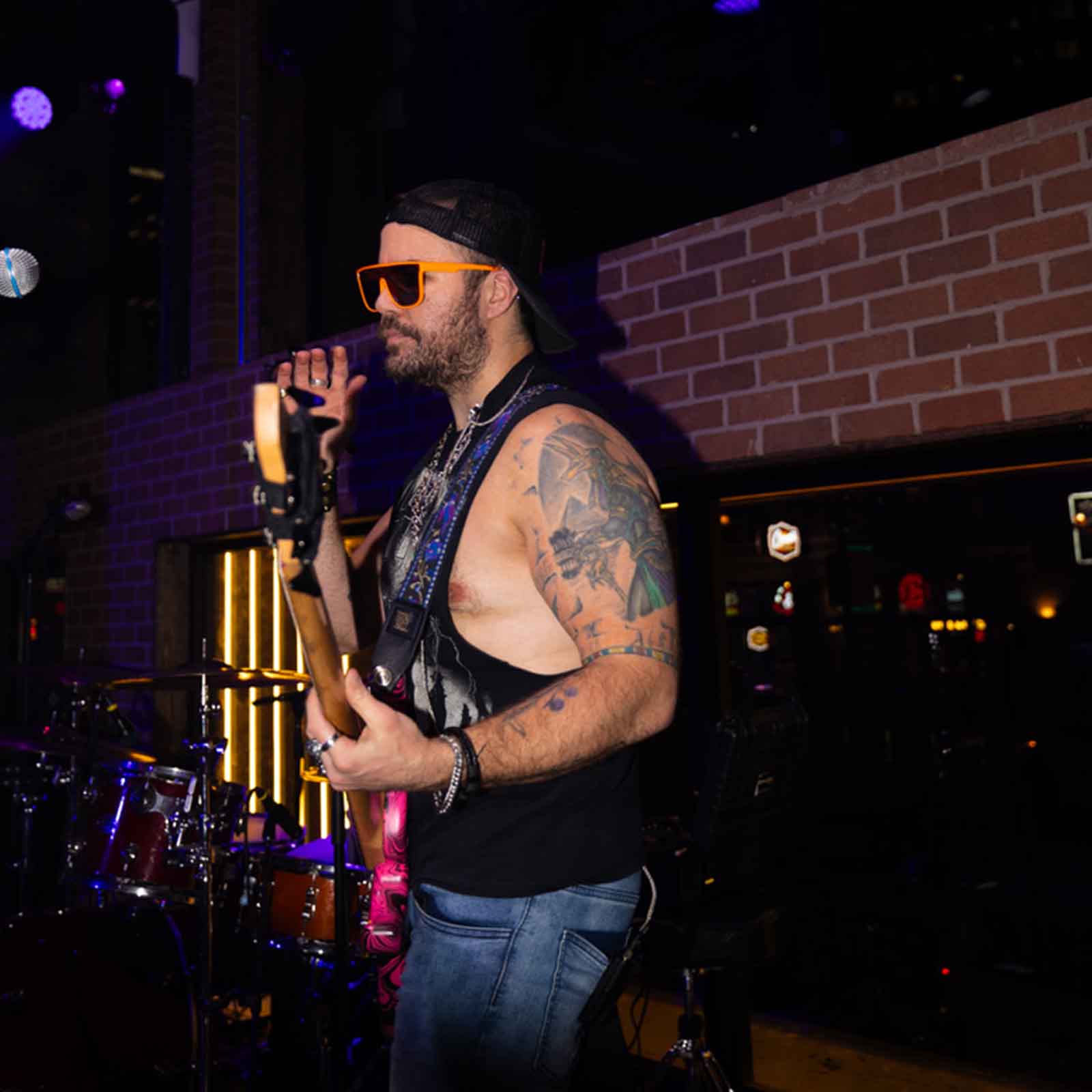 Guitarist performing on stage with a microphone and drums in the background.