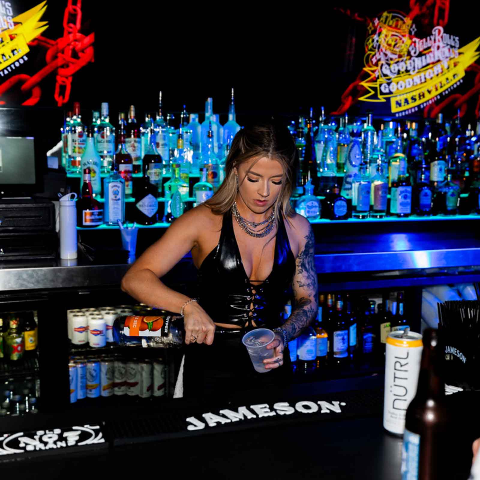 Bartender preparing a drink behind a well-stocked bar with neon lighting and Jameson branding.