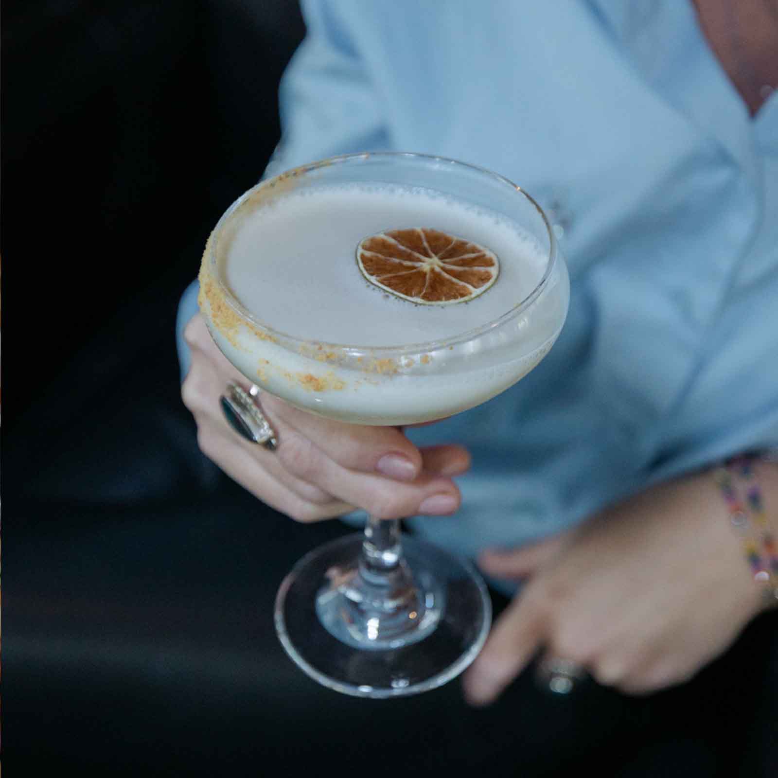 A cocktail with a dried lime garnish, served in a coupe glass. The drink has a frothy top and a rimmed sugar edge.