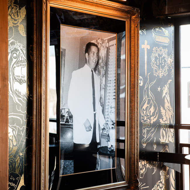 Portrait features Buddy's father in a suit printed in black and white framed in gold prominently displayed in Buddy's Backroom.