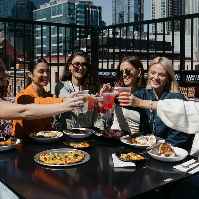 A lovely group of friends savoring an exquisite array of brunch and cocktail options on a gorgeous morning atop the rooftop of Goodnight Nashville.