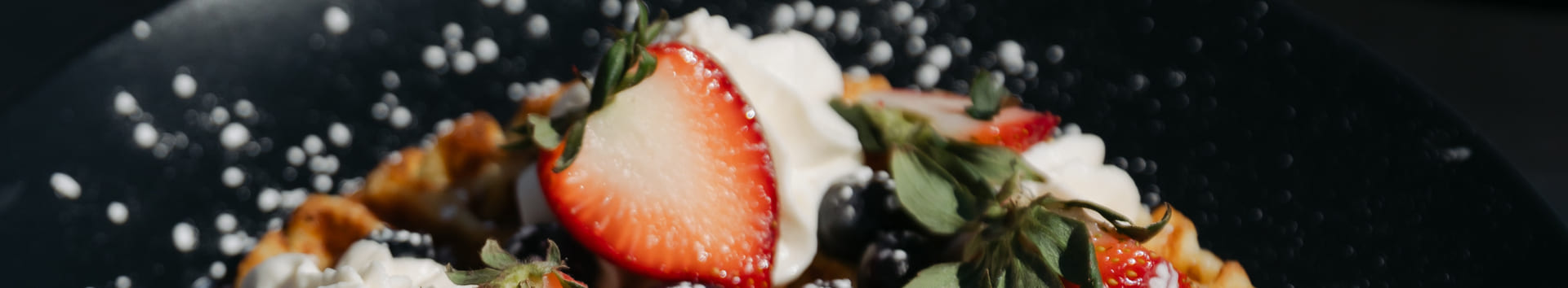 Waffle topped with whipped cream, fresh strawberries, blueberries, and powdered sugar on a black plate.