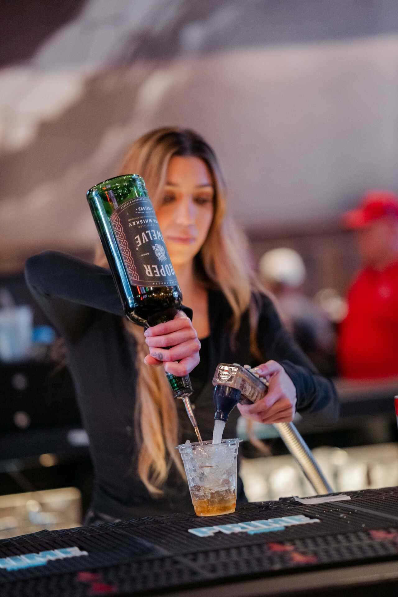 Bartender pouring liquor and soda into a plastic cup behind a bar.