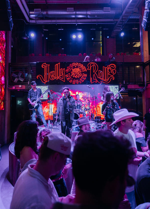 Live band performing on stage beneath a neon “Jelly Rolls” sign while a crowd watches inside a lively bar and music venue.
