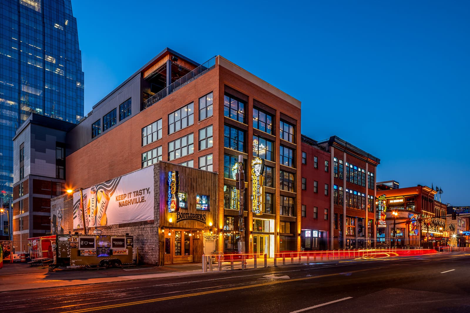 Exterior view of Goodnight Nashville on Nashville’s Broadway entertainment district at dusk, featuring illuminated signage, surrounding nightlife venues, and city street lights.