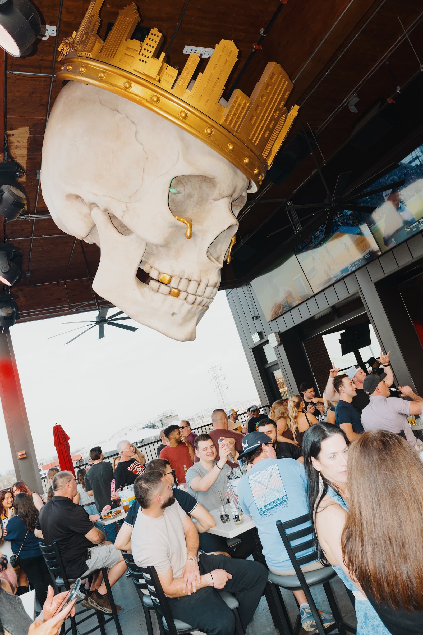 Guests gathered at a rooftop bar in Nashville beneath a large decorative skull sculpture with a gold city skyline crown, overlooking the Broadway entertainment district.